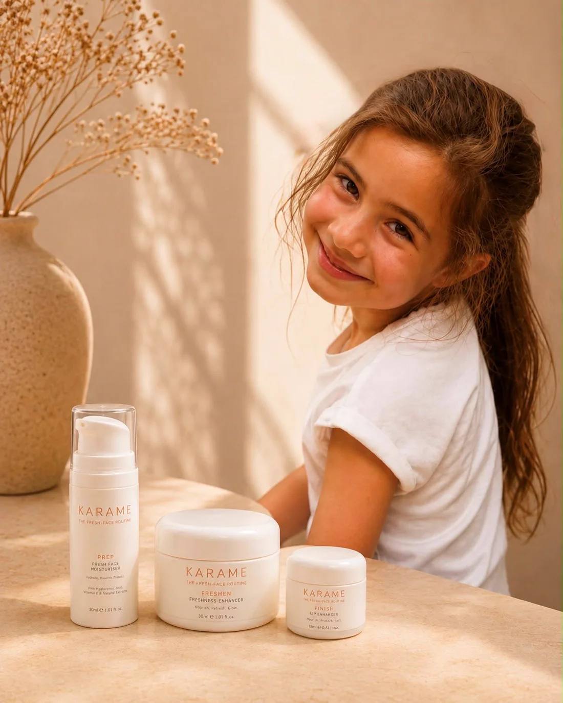A young girl smiling beside the three KARAME products on a sunlit table